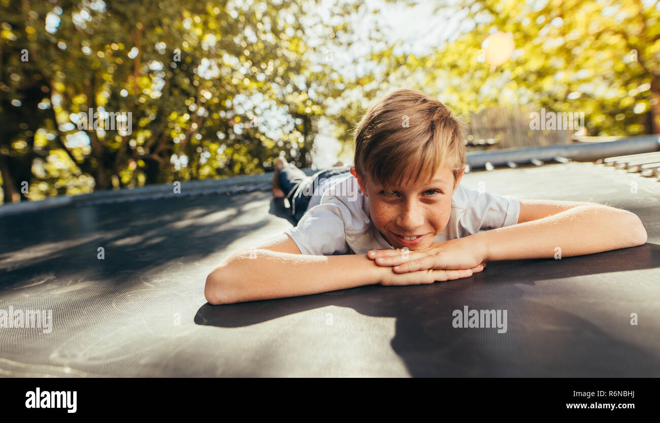 Petit garçon reposant sur trampoline après avoir joué à l'extérieur. Kid couché à l'avant sur un trampoline et souriant. Banque D'Images