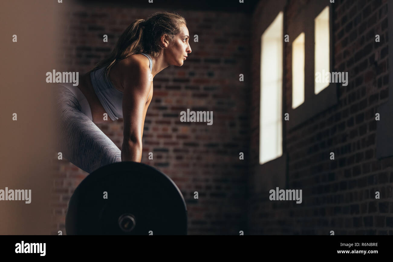 Femme fitness déterminé la formation avec des poids lourds en club de remise en forme. Athlète féminine caucasienne de levage de poids faire de l'exercice dans la salle de sport. Vue de côté. Banque D'Images