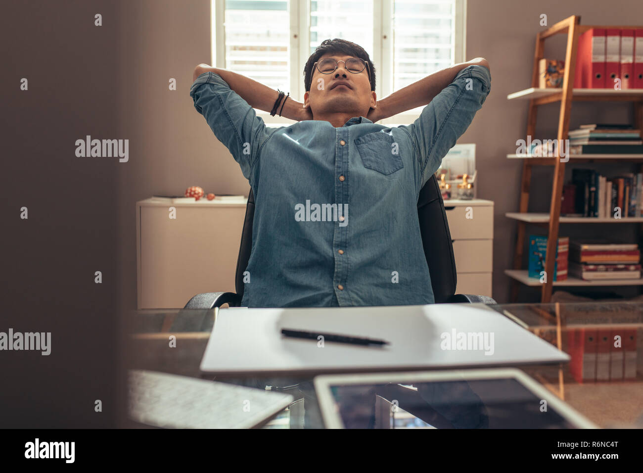 Professionnel de la création assis à son bureau, confortablement assis dans un fauteuil avec les mains derrière la tête et les yeux fermés. Designer prendre pause du travail à son bureau. Banque D'Images