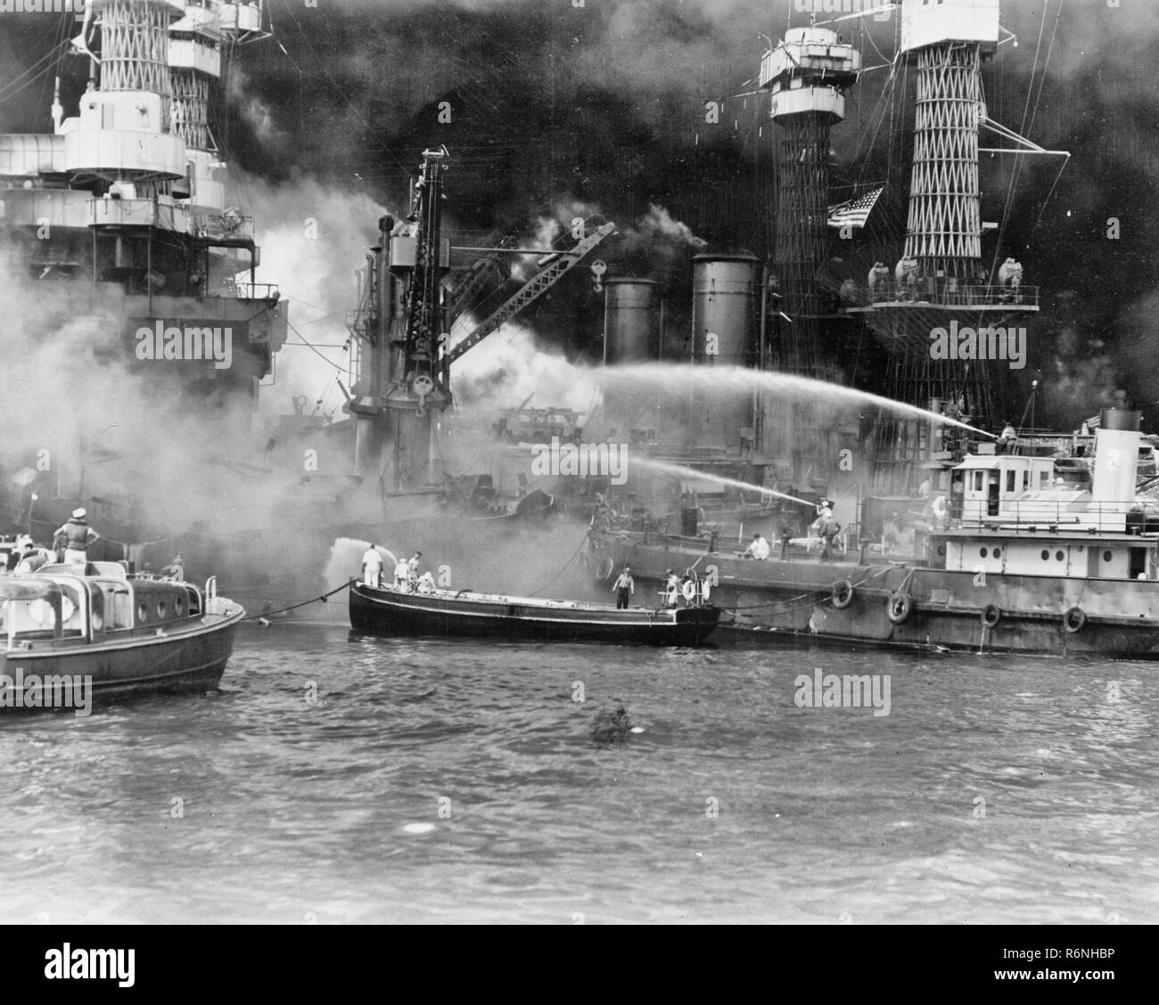 Attaque de Pearl Harbor, Hawaii. USS West Virginia en feu. Sans tenir compte de la possibilité d'explosions dangereuses, United States marins homme leurs bateaux sur le côté de l'incendie, cuirassé USS West Virginia, pour mieux lutter contre les flammes ont commencé par torpilles japonaises et des bombes. Remarque Les couleurs nationales voler contre le ciel noirci de fumée Banque D'Images