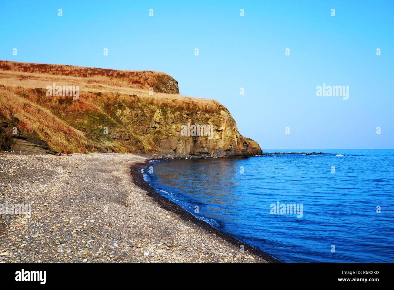 De grosses pierres sèches avec de l'herbe d'automne sur la toile de fond de la mer. Sur le littoral et dans l'eau bleu vif. Un rocher se reflète sur la surface de l'eau. Ea Banque D'Images