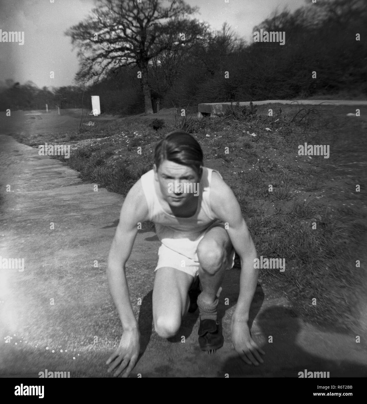 1940, historique, un jeune homme dans son kit d'athlétisme à genoux à l'extérieur, dans une pose que si le démarrage d'une course de sprint, Essex, Angleterre. Banque D'Images