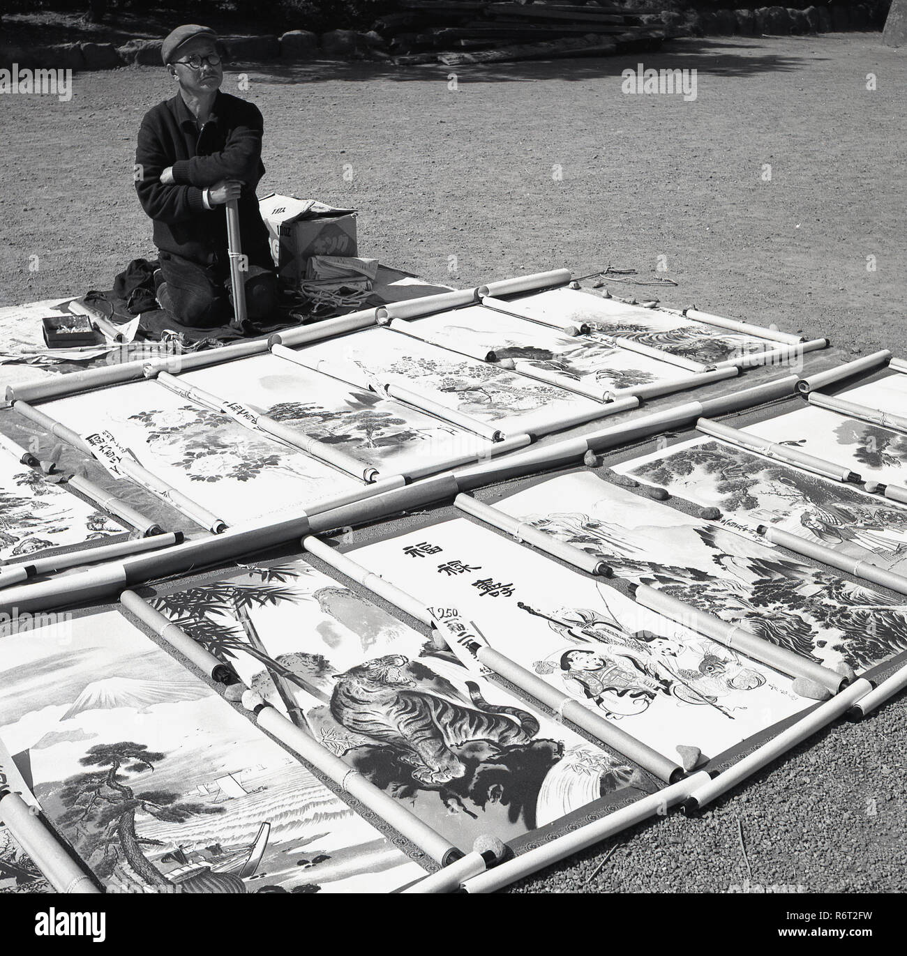 Années 1960, historique, un artiste japonais à l'extérieur de genou sur le sol avec ses oeuvres - hanging scroll imprime - sur l'affichage. Banque D'Images