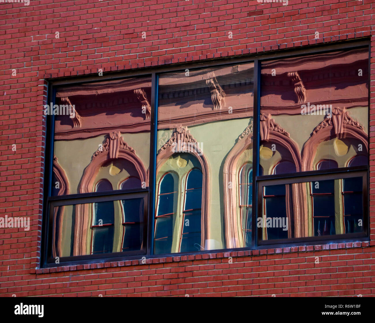 Tôt le matin, heure d'Or présente les réflexions d'un bâtiment en face de la rue dans les fenêtres de ce bâtiment en brique Troy New York. Banque D'Images