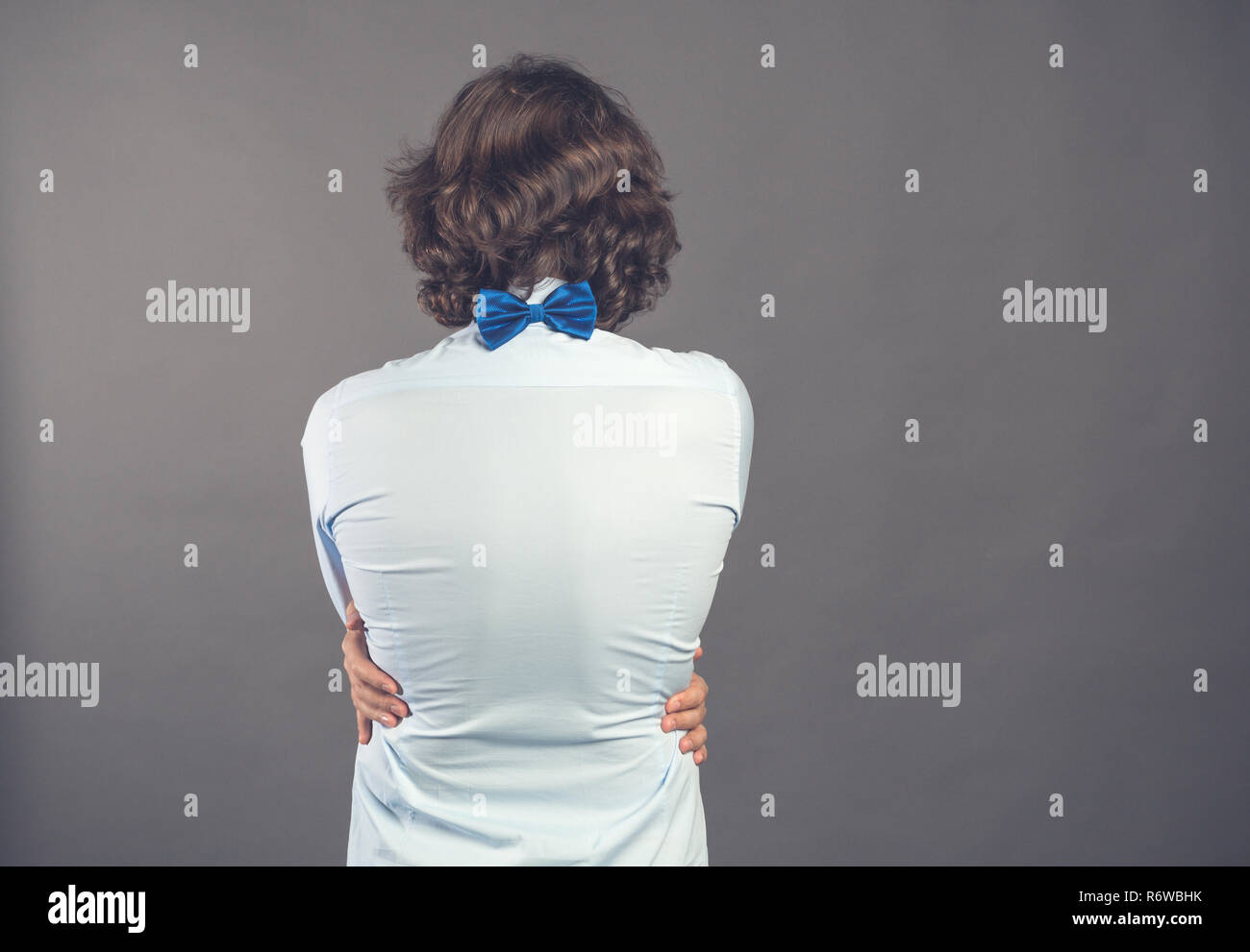 Jeune homme en chemise bleu et dentelle épouse lui-même sur fond gris. Vue arrière. Ses mains se trouvent sur la taille. Il a besoin d'être embrassé. Sentiment égoïste, l'amour vous-même concept. Les émotions positives. Copy space Banque D'Images