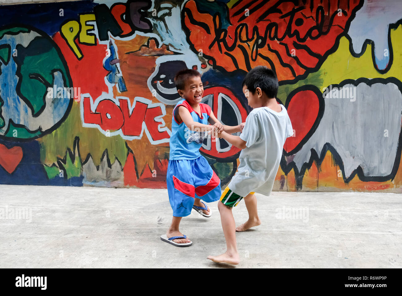 Les enfants de la rue enfants tournent en face d'un mur de graffiti à l'Kuya Center pour les enfants de la rue à Quezon City, Metro Manila, Philippines. Banque D'Images