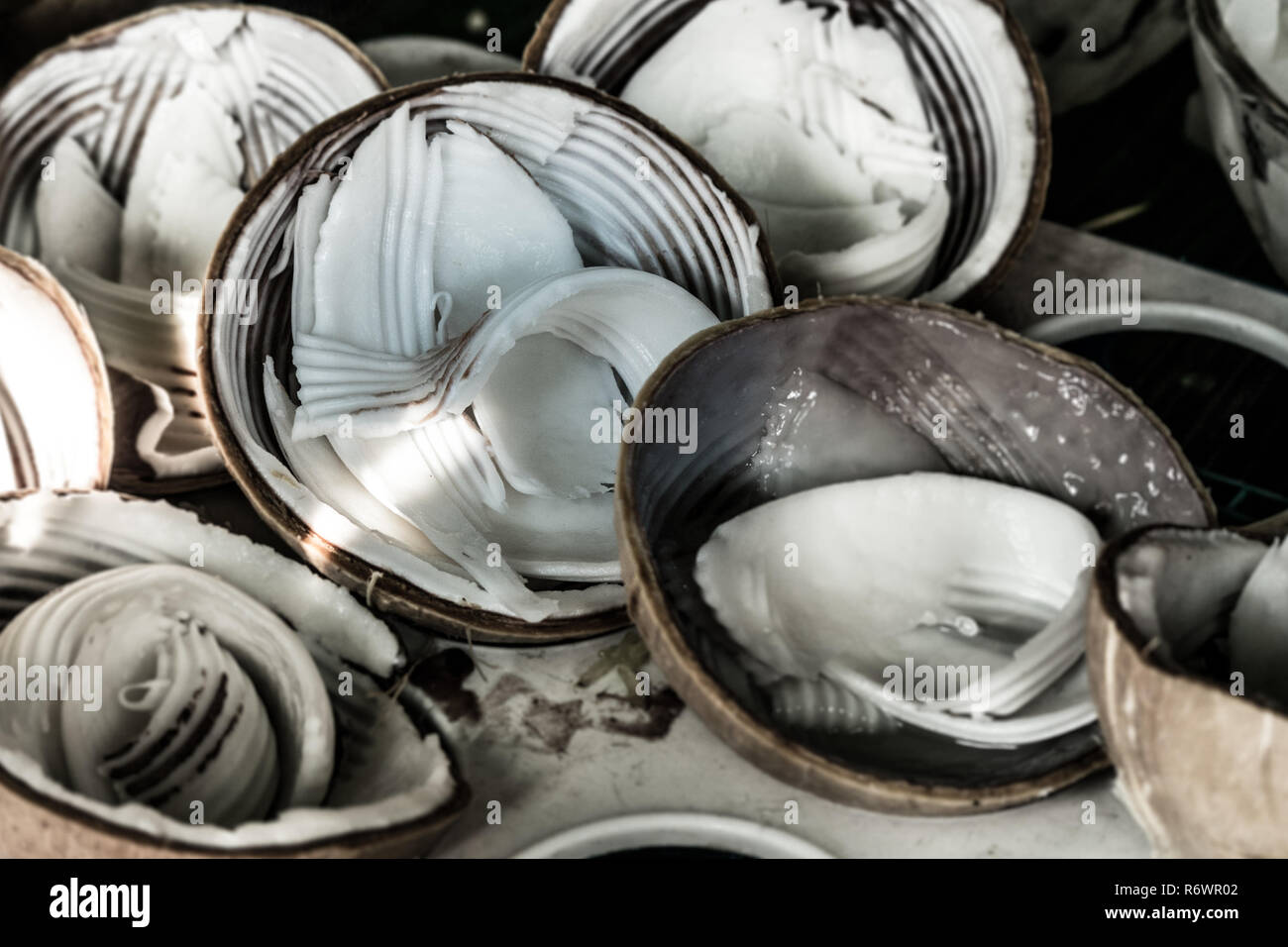 Jeune chair de noix de coco fraîches grattées dans leurs moitiés shell prêt à manger à la vente à un vendeur de rue. Banque D'Images