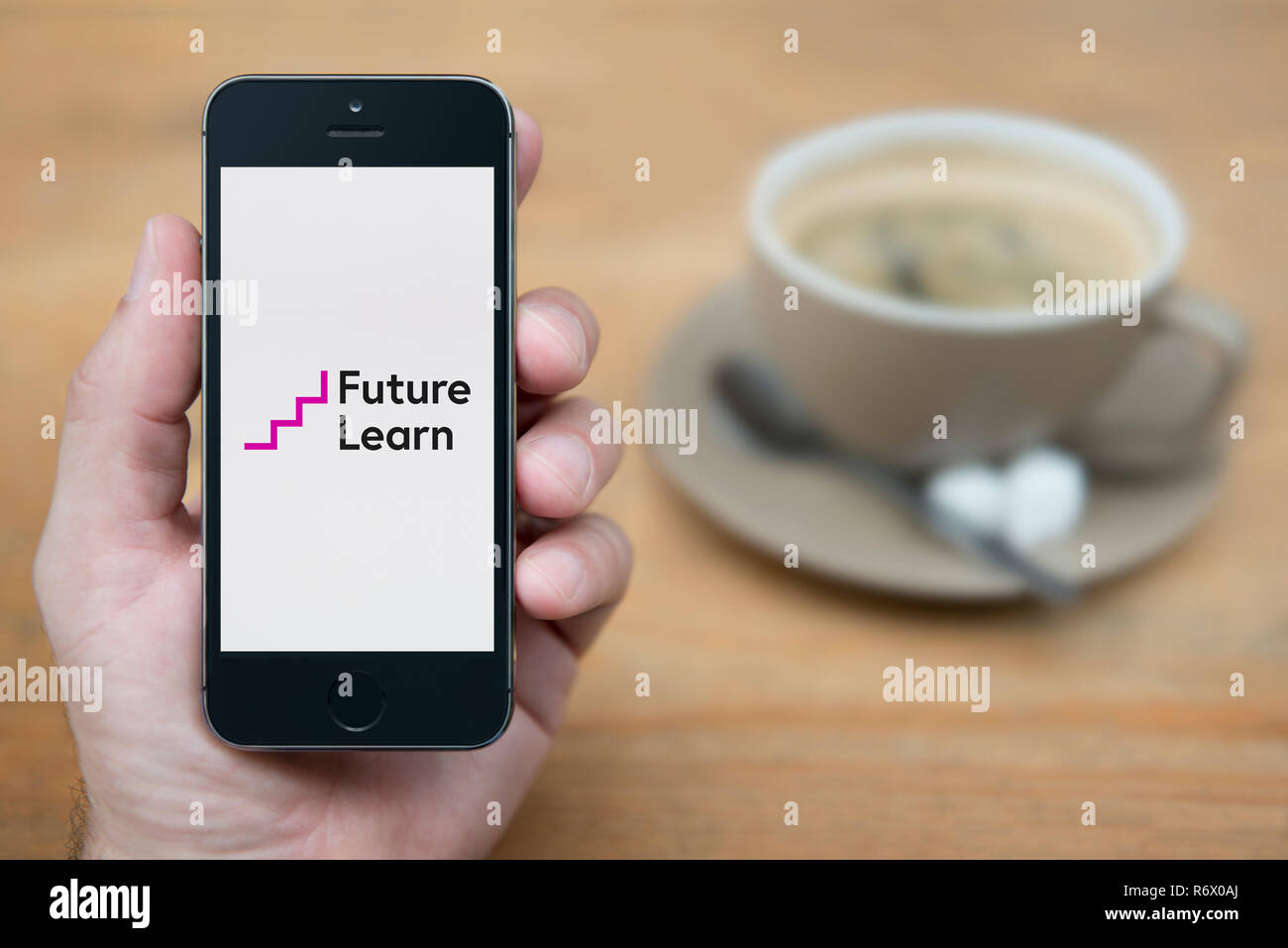Un homme se penche sur son iPhone qui affiche l'avenir apprendre logo (usage éditorial uniquement). Banque D'Images
