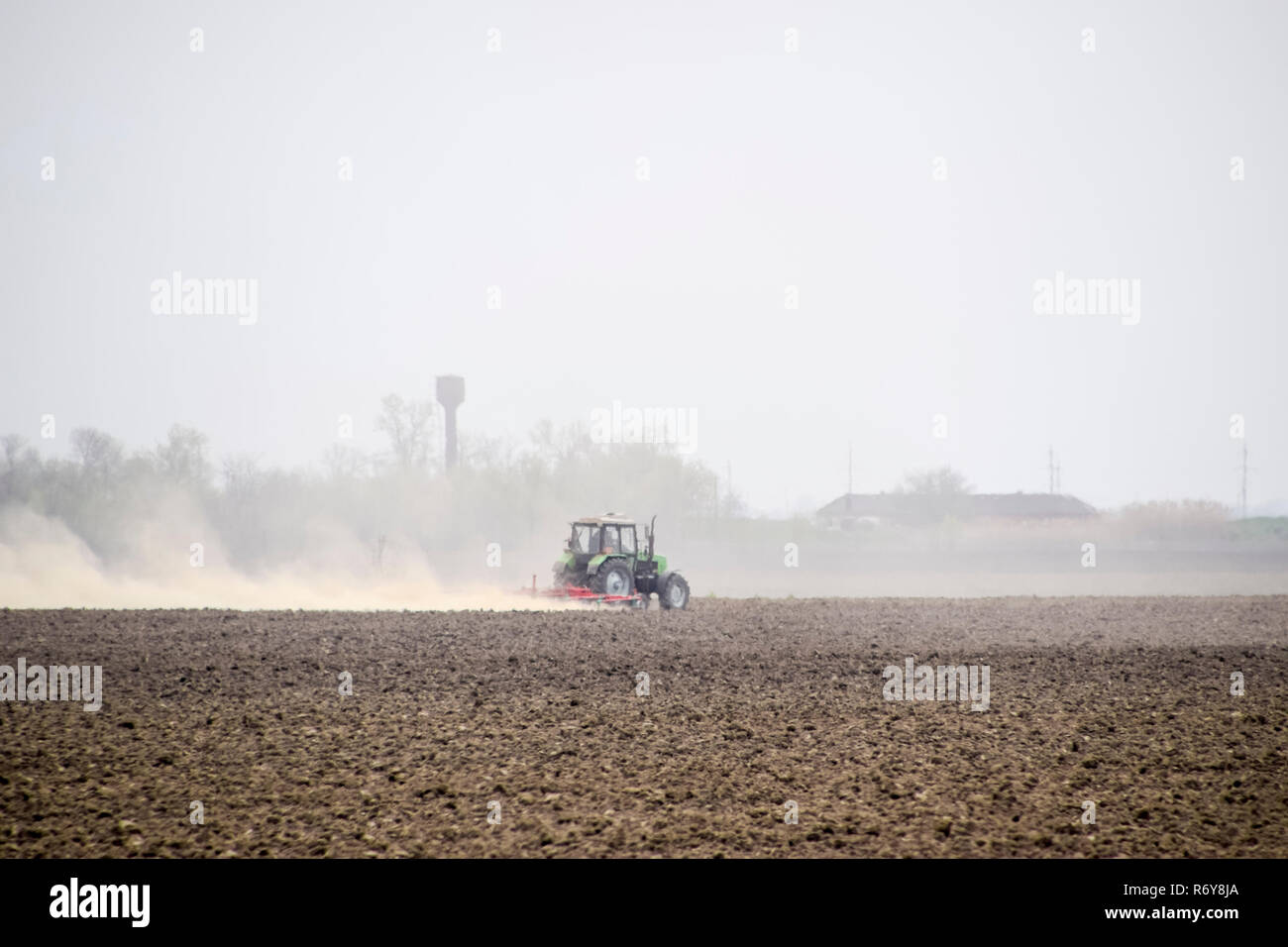 Le tracteur herse le sol sur le terrain et crée un nuage de poussière derrière elle Banque D'Images