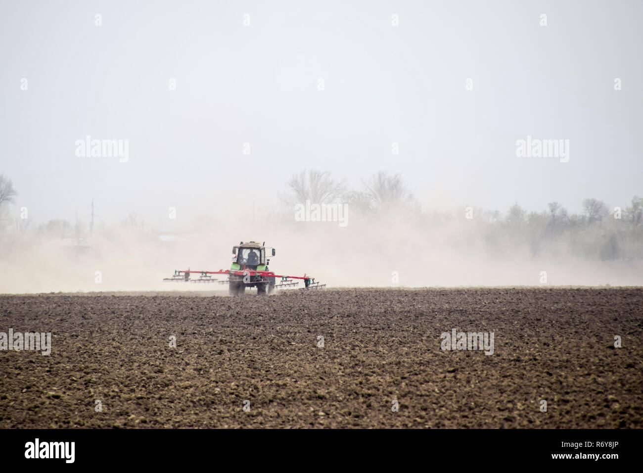 Le tracteur herse le sol sur le terrain et crée un nuage de poussière derrière elle Banque D'Images