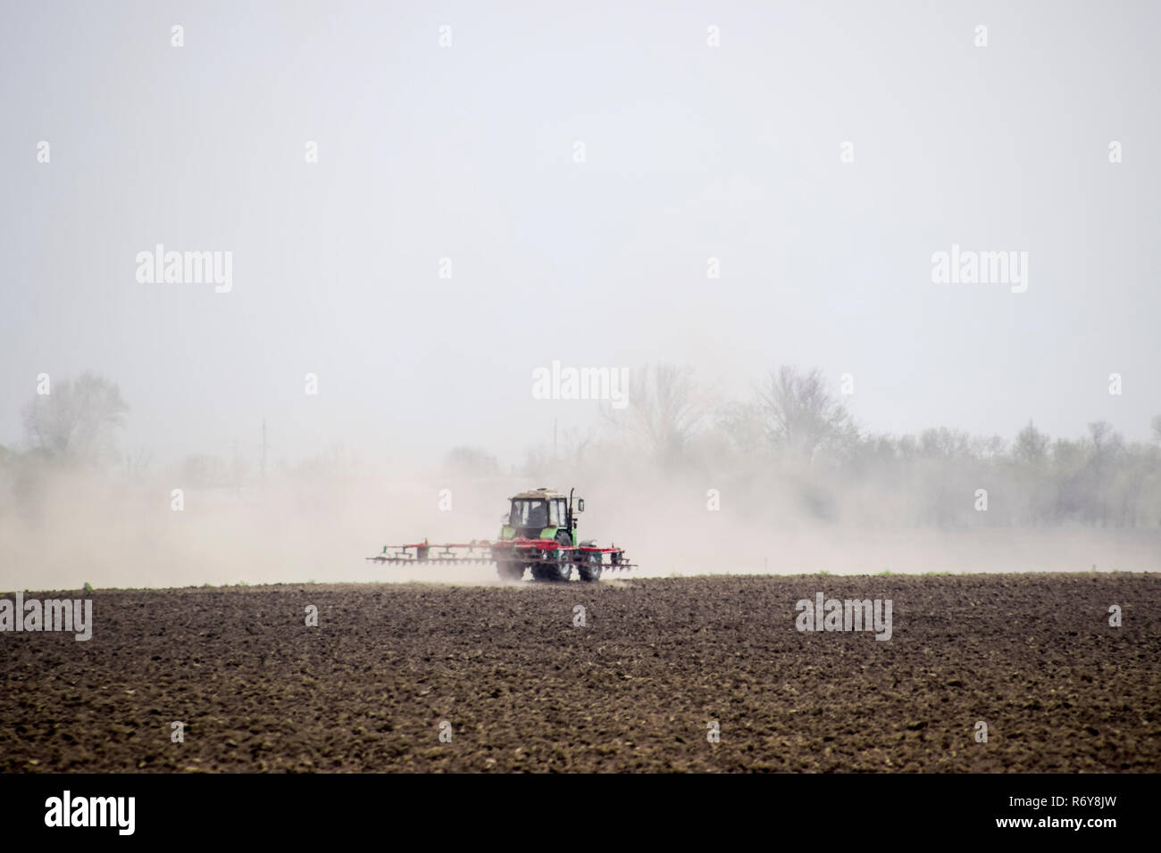 Le tracteur herse le sol sur le terrain et crée un nuage de poussière derrière elle Banque D'Images