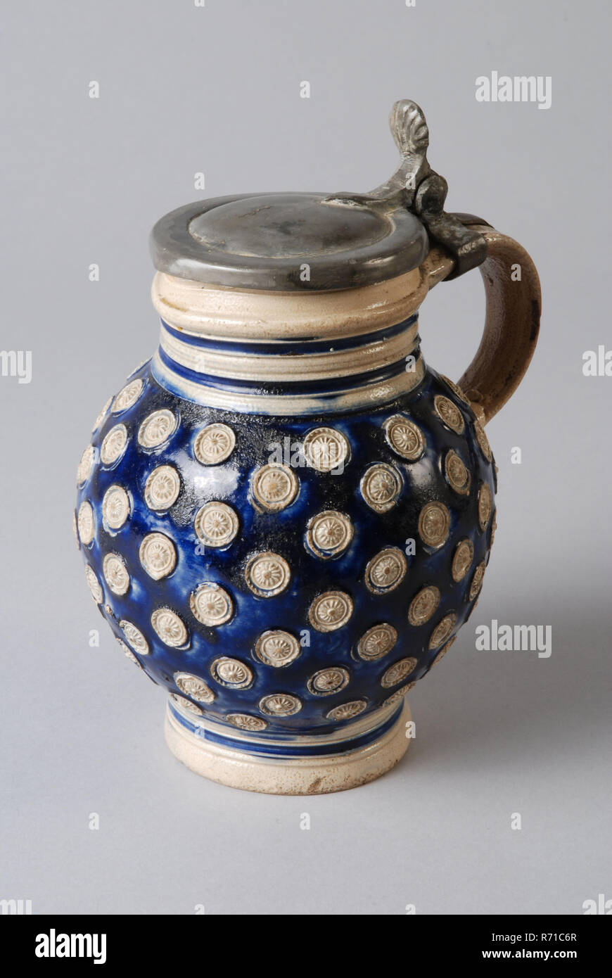 Cloche en grès à pied, entièrement recouvert de petites rosettes, les appliqués, couvercle étain, bullet-bell jar titulaire de la vaisselle en grès céramique trouver sol glaze glaçure sel de métal d'étain, tournées à la main estampillé vitrage vitrage grès cuits au four avec la base de bell jar sur le cou cylindrique court. Couvercle en étain inaperçue et peut-être pas l'oreille à profil original recroquevillée sur la pièce jointe avec le ventre anneaux Profil autour du cou et le pied se précipitant bleu complètement couverte de petites rosettes d'appliqués sur fond bleu cobalt archéologie poterie autochtone potable d'importation pour le service du vin bière Banque D'Images