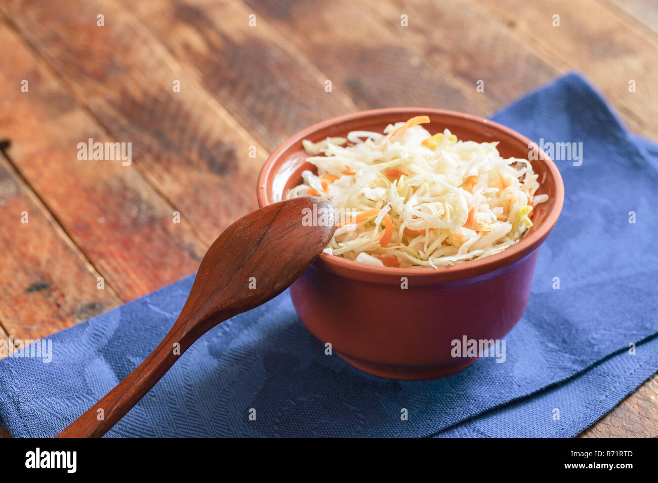 Brown pot en argile avec de la choucroute et cuillère en bois sont debout sur une serviette de cuisine bleu sur table en bois. Banque D'Images