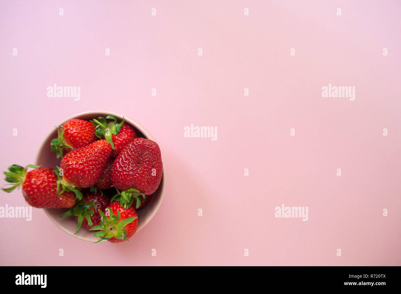 Haut de voir des fraises fraîches dans un bol rose sur fond rose. Banque D'Images