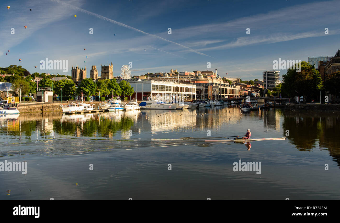 Bristol, Angleterre, Royaume-Uni - 11 août 2018 : un rameur en trains Bristol's docks port flottant sur un matin d'été, alors que des ballons à air chaud flotter au-dessus de la c Banque D'Images