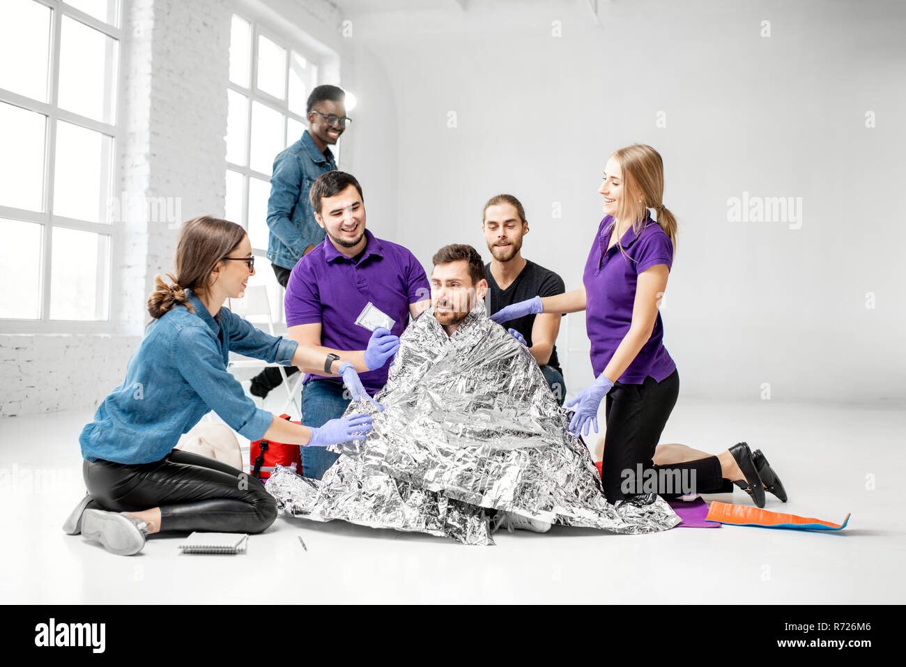 Personnes au cours de la formation aux premiers secours avec les instructeurs et l'homme en tant que personne visée dans une couverture thermique à l'intérieur Banque D'Images