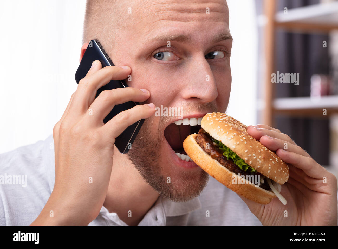 Portrait of a Young Man Talking On Mobile Phone while eating Hamburger Banque D'Images