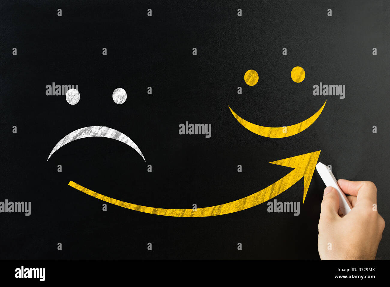 Close-up de la main d'un homme à partir de la flèche dessin triste de visage heureux sur tableau noir Banque D'Images