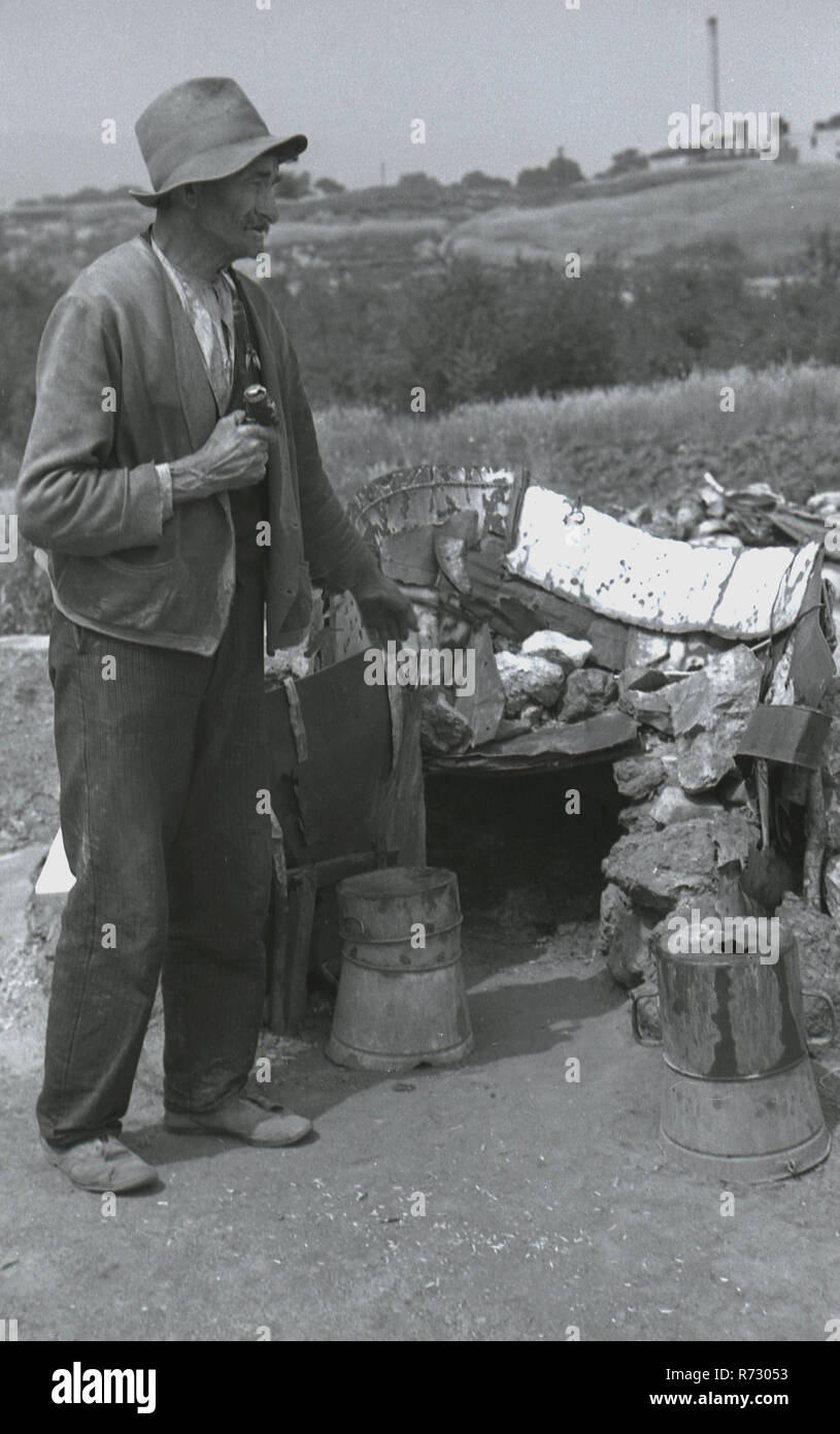 Années 1930, historiques, de la Tchécoslovaquie, sudentenland, pré-ww2 et un homme débraillé avec son longpipe Bavarois aux portes d'une baraque de bas niveau dans un terrain accidenté, plus peut-être un sans-abri, un peson ou vagabond. Banque D'Images