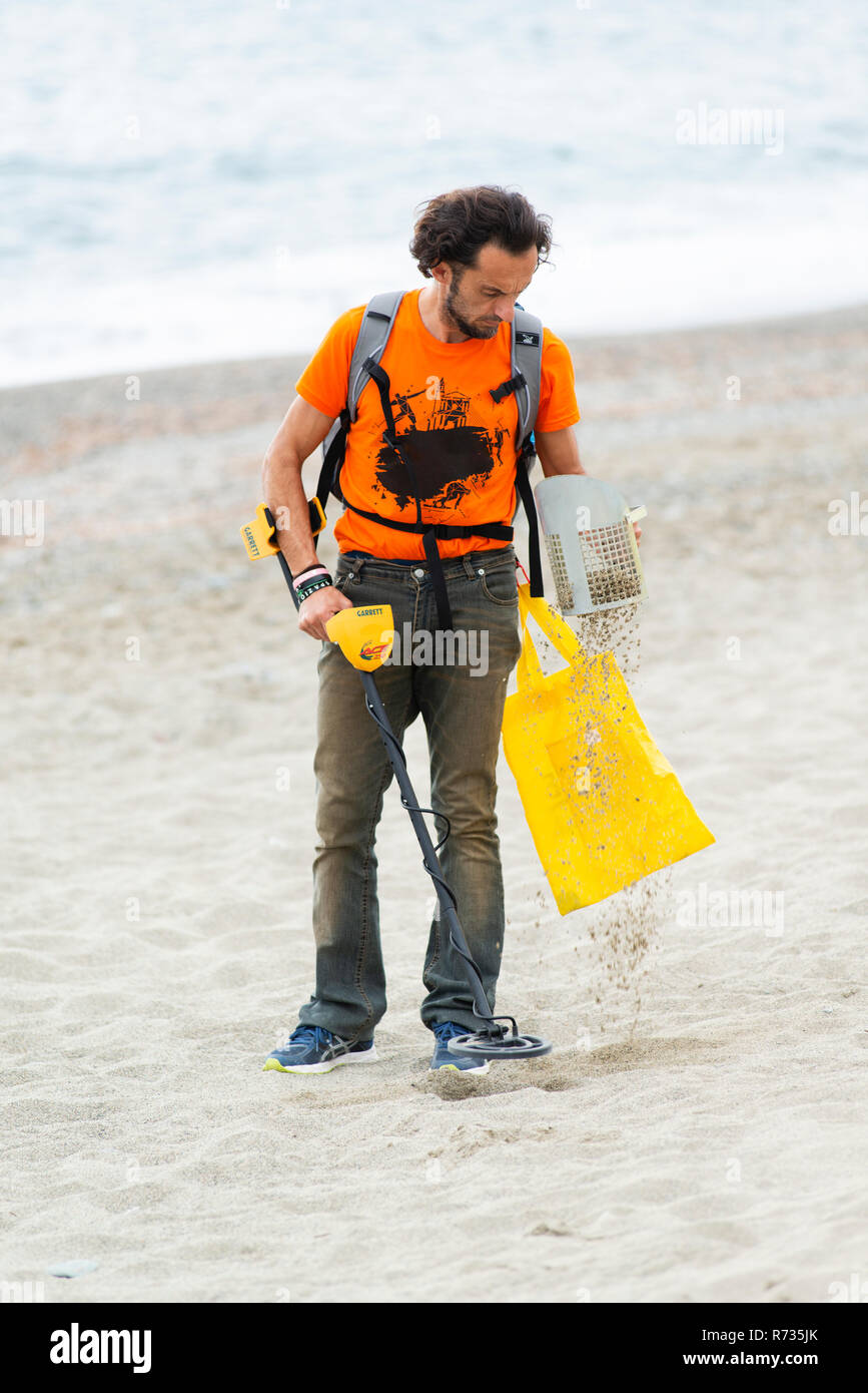 Savona, Italie, 25 Octobre 2018 : l'homme est la marche sur la plage avec un détecteur de métaux dans une main et un tamis dans l'autre. Il essaie de trouver des lunet Banque D'Images