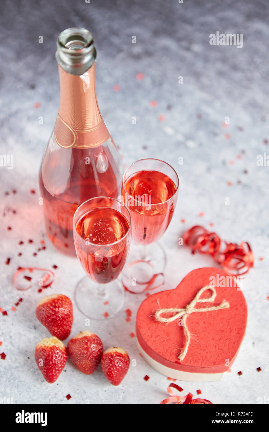 Bouteille de champagne rose, les verres avec des fraises fraîches et des cadeaux en forme de coeur Banque D'Images