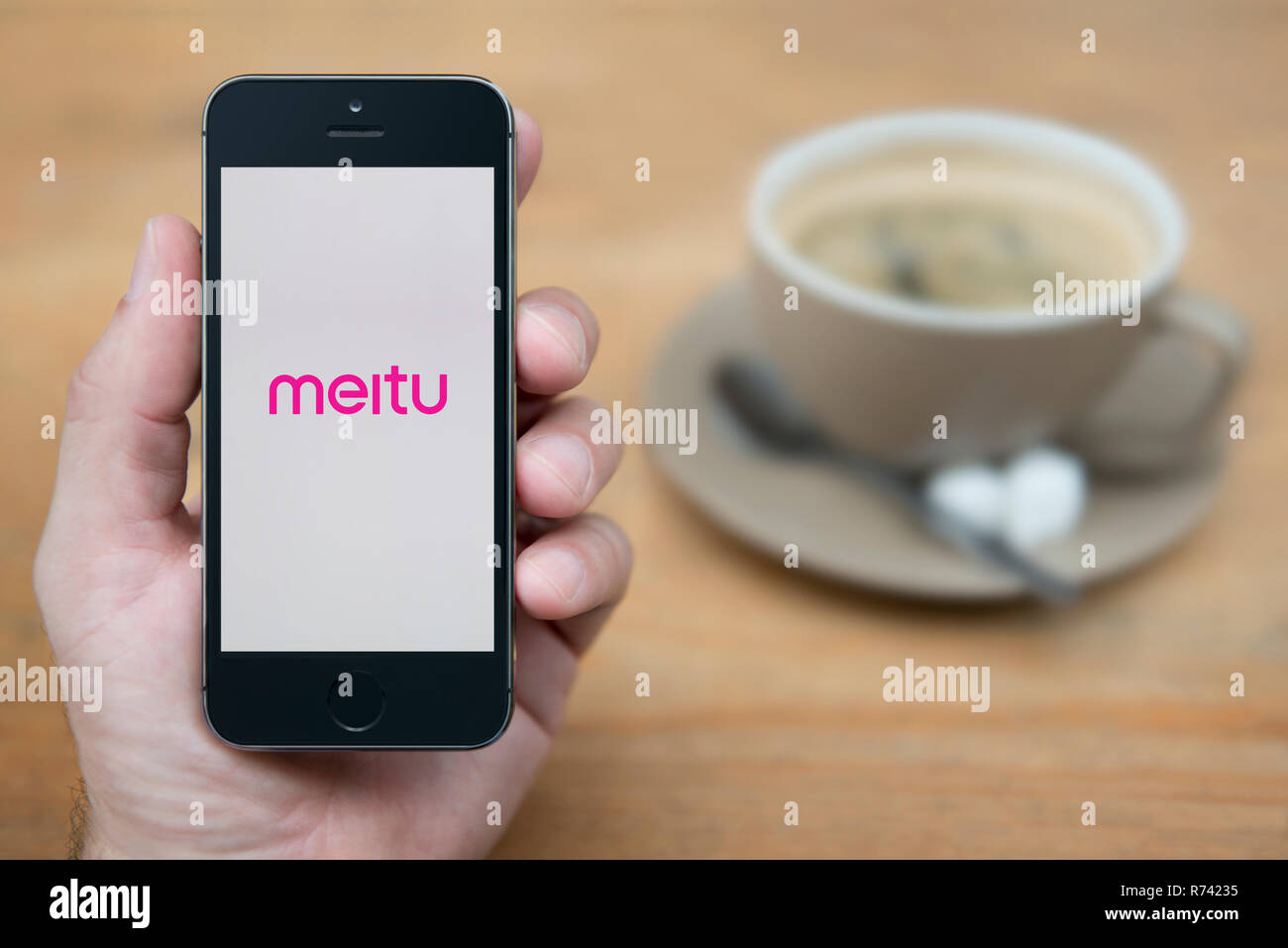 Un homme se penche sur son iPhone qui affiche le logo Meitu (usage éditorial uniquement). Banque D'Images