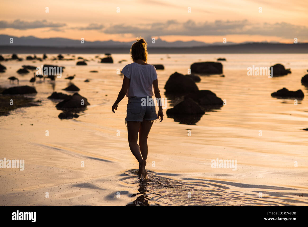 Jeune femme à la cheville dans l'eau au coucher du soleil, l'île de Quadra, Campbell River, Canada Banque D'Images