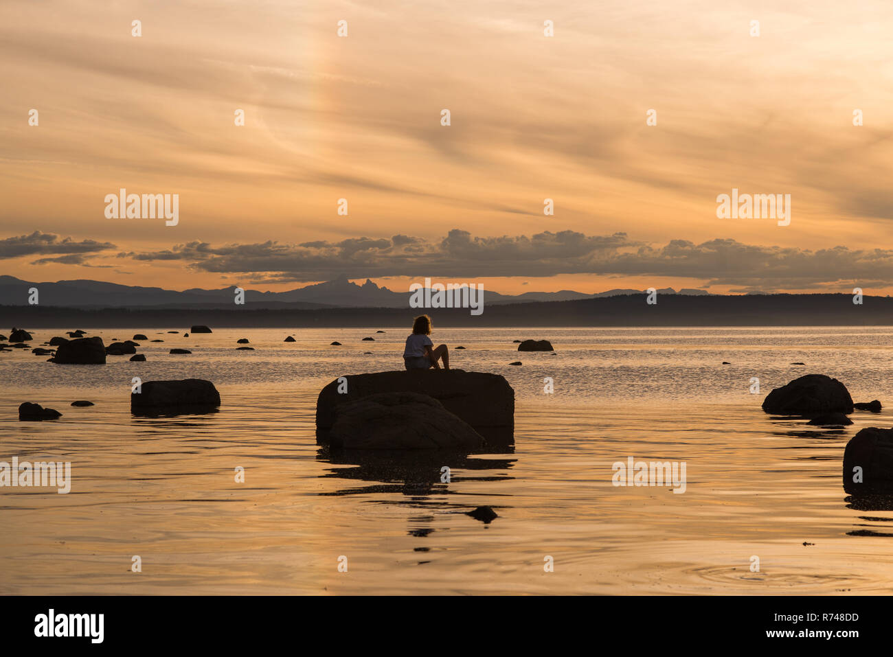 Young woman sitting on rock au coucher du soleil, l'île de Quadra, Campbell River, Canada Banque D'Images