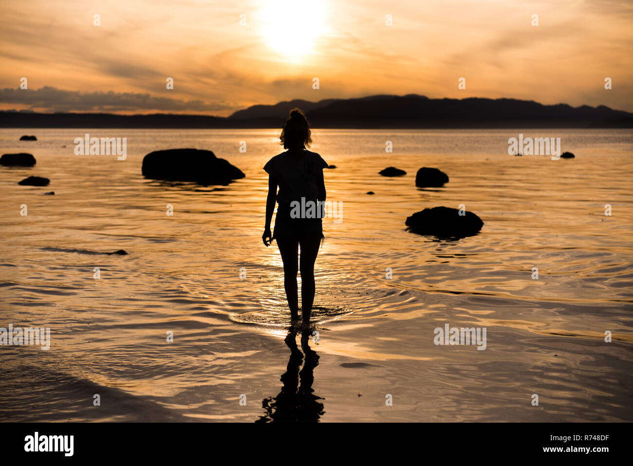 Young woman looking out au coucher du soleil, en silhouette vue arrière, Quadra Island, Campbell River, Canada Banque D'Images