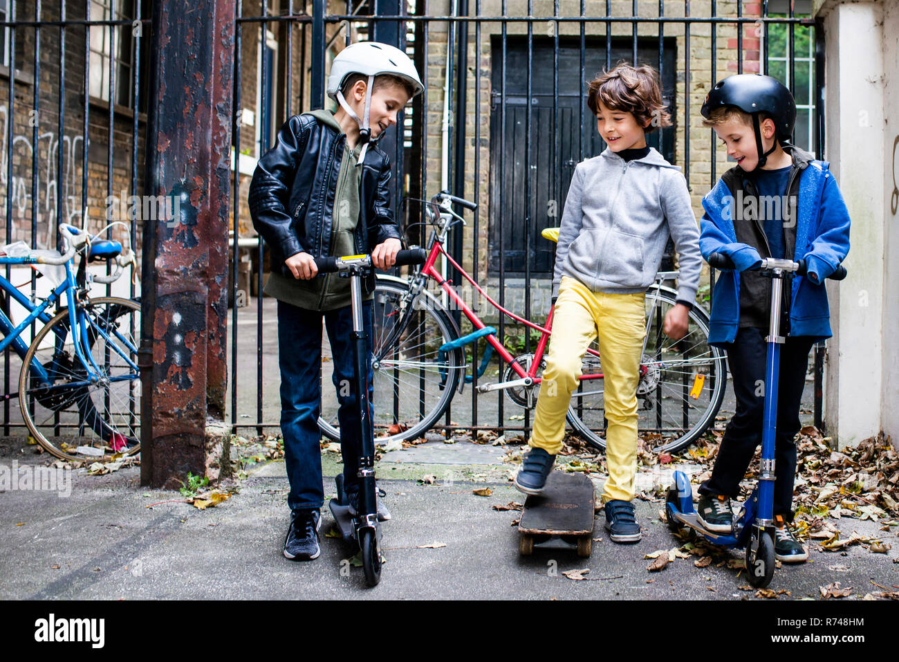 Les garçons équitation pousser scooter et du skateboard, vélos en arrière-plan Banque D'Images