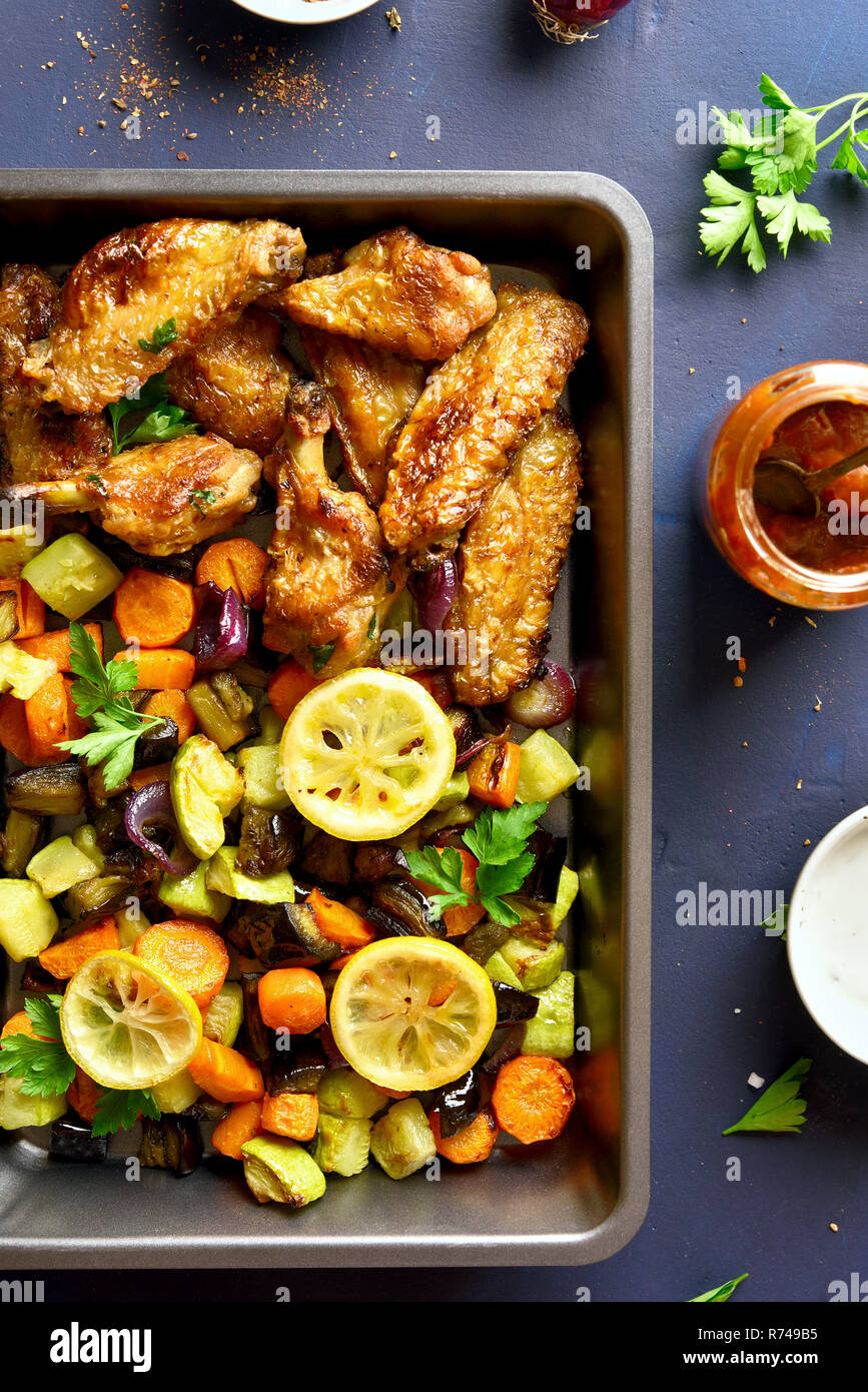 Ailes de poulet avec légumes frits dans la lèchefrite sur fond noir en bleu. Haut de la vue, télévision lay Banque D'Images