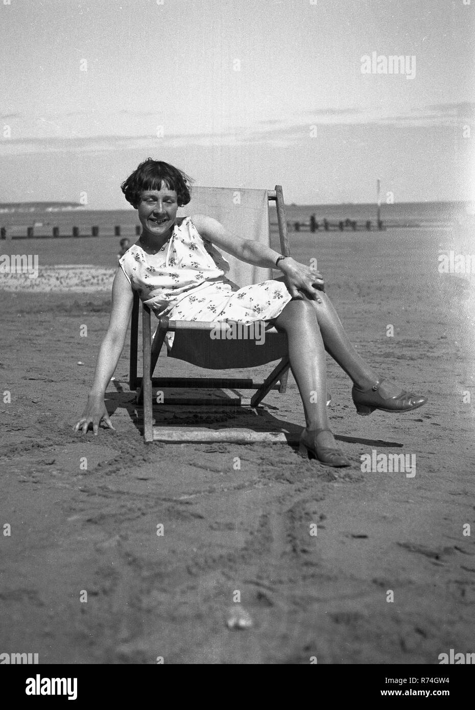 Années 1930, historiques, jeune femme dans une chaise longue sur une plage de sable. Banque D'Images