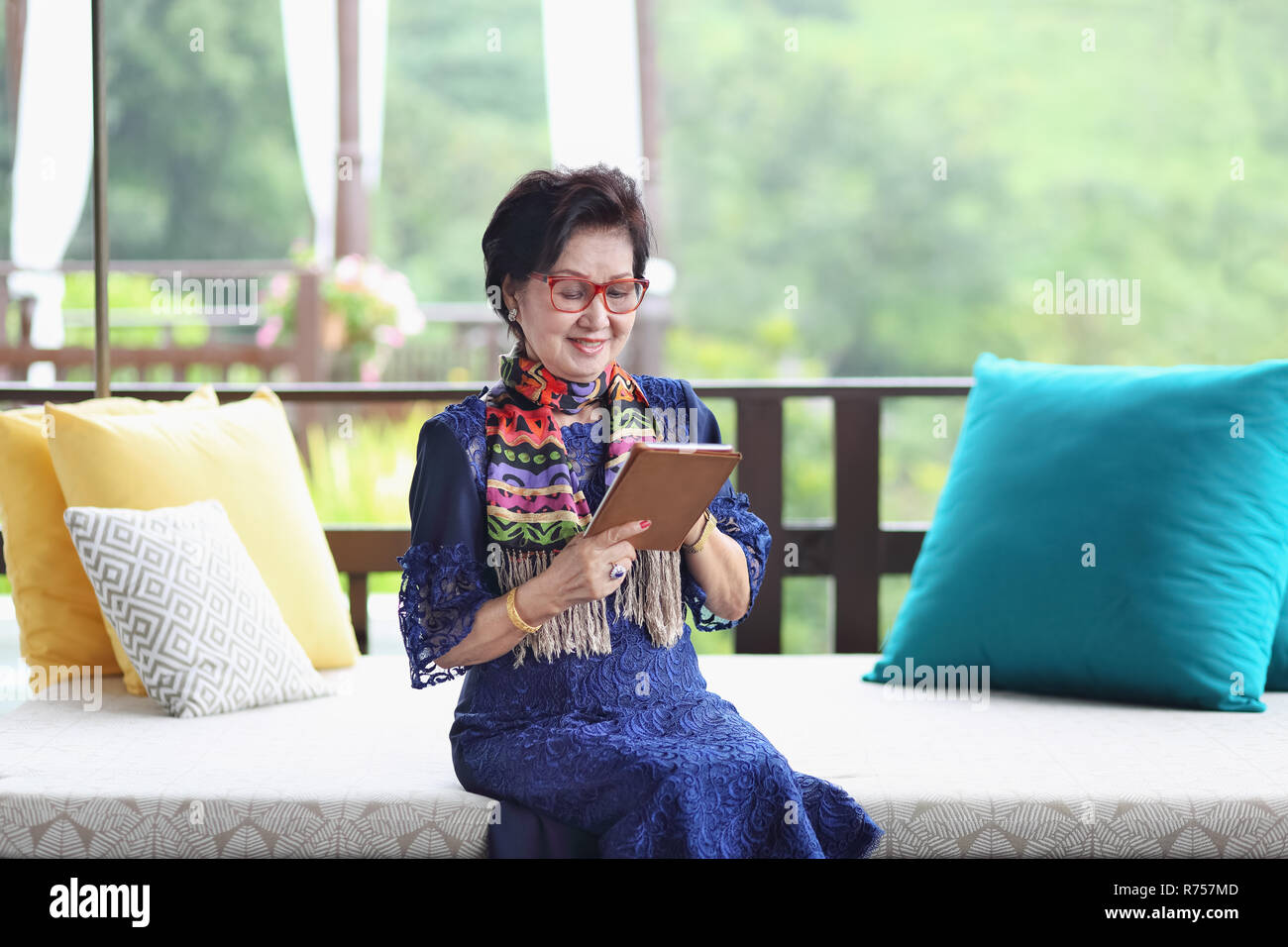 Asian senior femme assise sur le canapé et à l'aide d'une tablette Banque D'Images