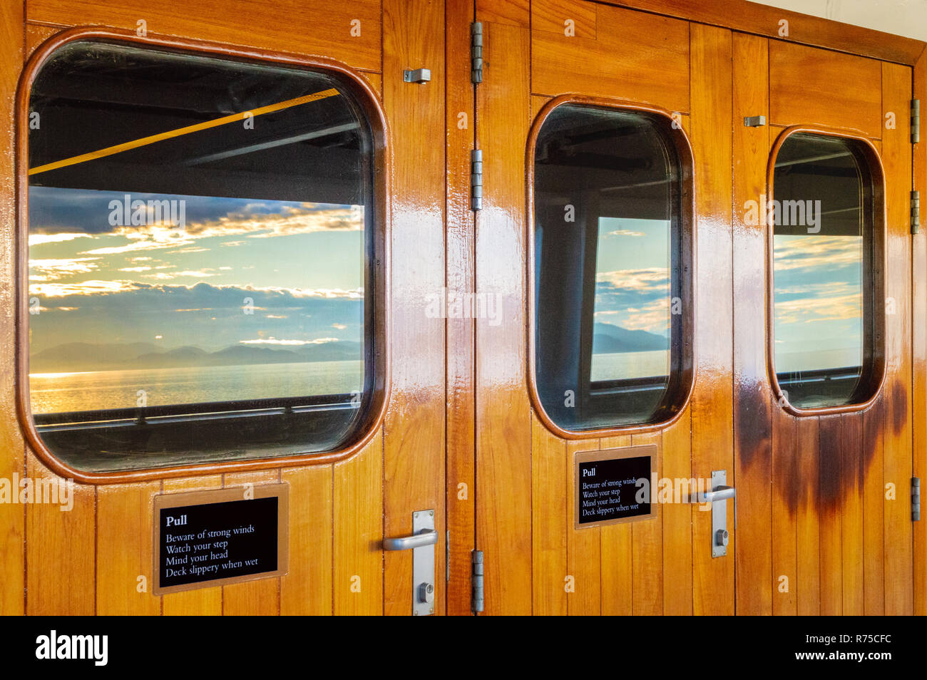 Vernis en bois lourds portes extérieures avec windows et réflexions de mer et soleil du matin dans des panneaux de verre sur un bateau de croisière. L'Alaska, USA. Banque D'Images