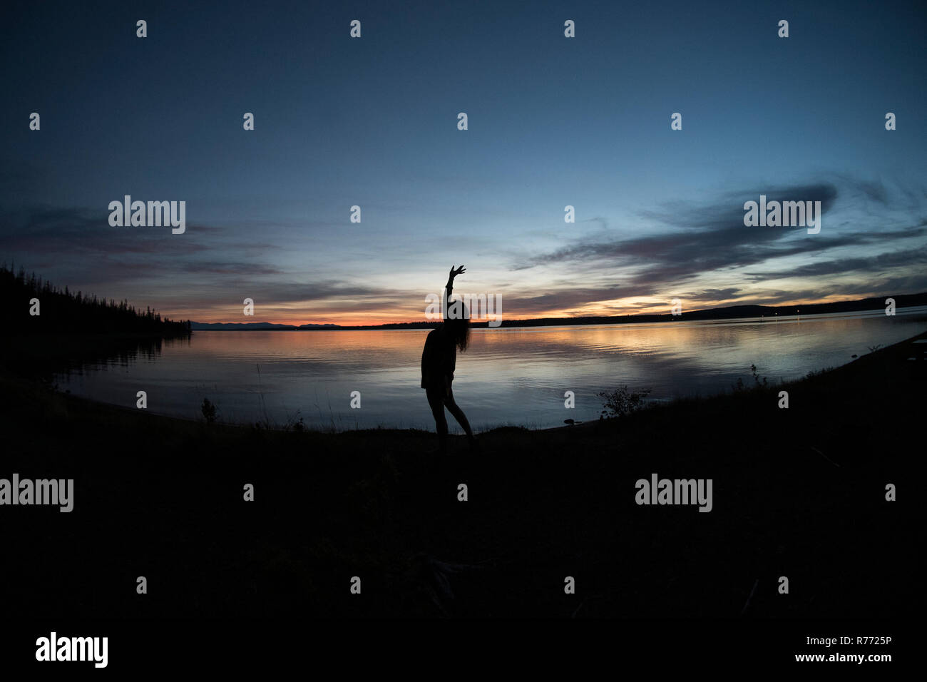 Image de grand angle en silhouette femme debout par l'eau, d'étirements et d'admirer l'horizon magnifiquement éclairée avec la paix et la solitude à Lakeside Banque D'Images