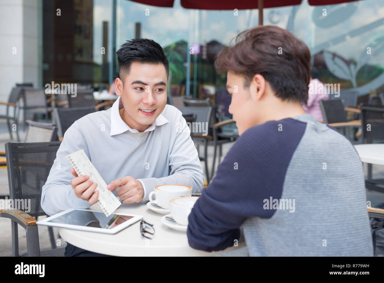 Deux jeunes hommes d'affaires dans les tenues de beau sourire, parler dans un café. Banque D'Images