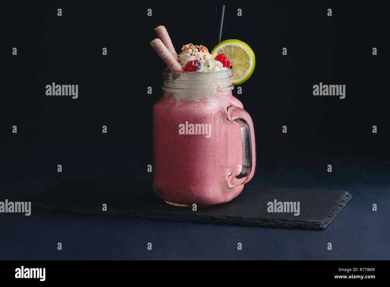 Milkshake fraise froide dans un verre vintage pot Mason. Fond sombre avec copie espace pour un menu. Banque D'Images