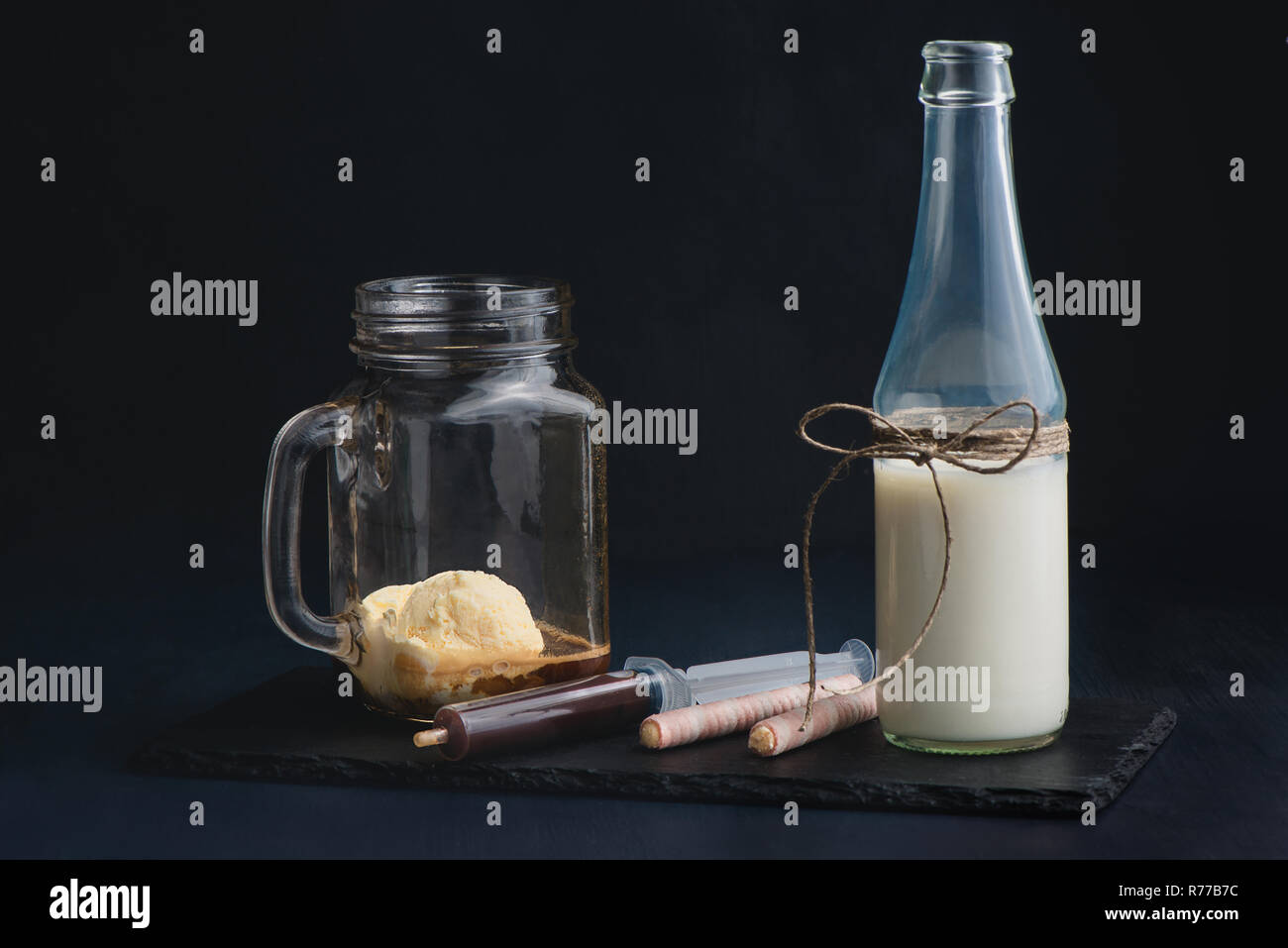 Cuillère à glace et une bouteille de lait préparé pour prendre un milk-shake dans un verre vintage pot Mason. Fond sombre avec copie espace pour un menu. Banque D'Images