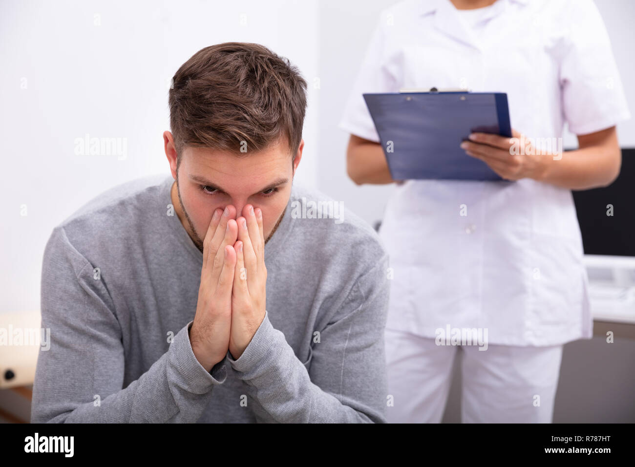 Close-up d'avoir des troubles de l'jeune homme assis en face de Doctor Holding Clipboard Banque D'Images
