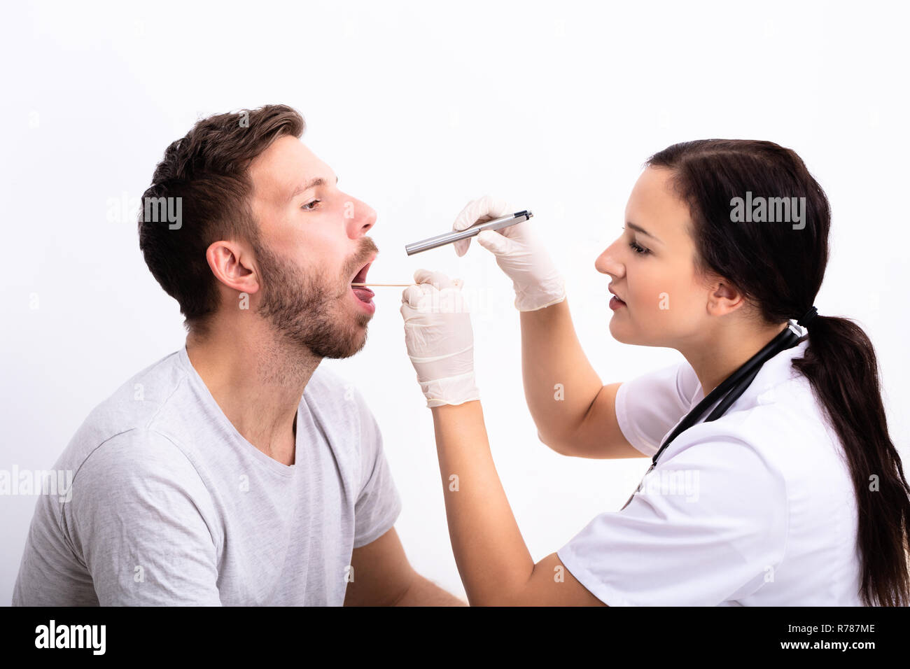 Jeune femme médecin Contrôle de l'homme mal de gorge avec abaisse-langue Banque D'Images