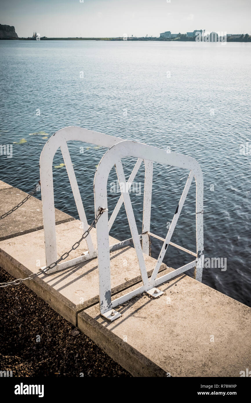 Mains courantes d'une échelle d'acier menant l'un du côté d'un trottoir de béton au bord de l'eau, dans la baie de Cardiff, Pays de Galles, Royaume-Uni Banque D'Images