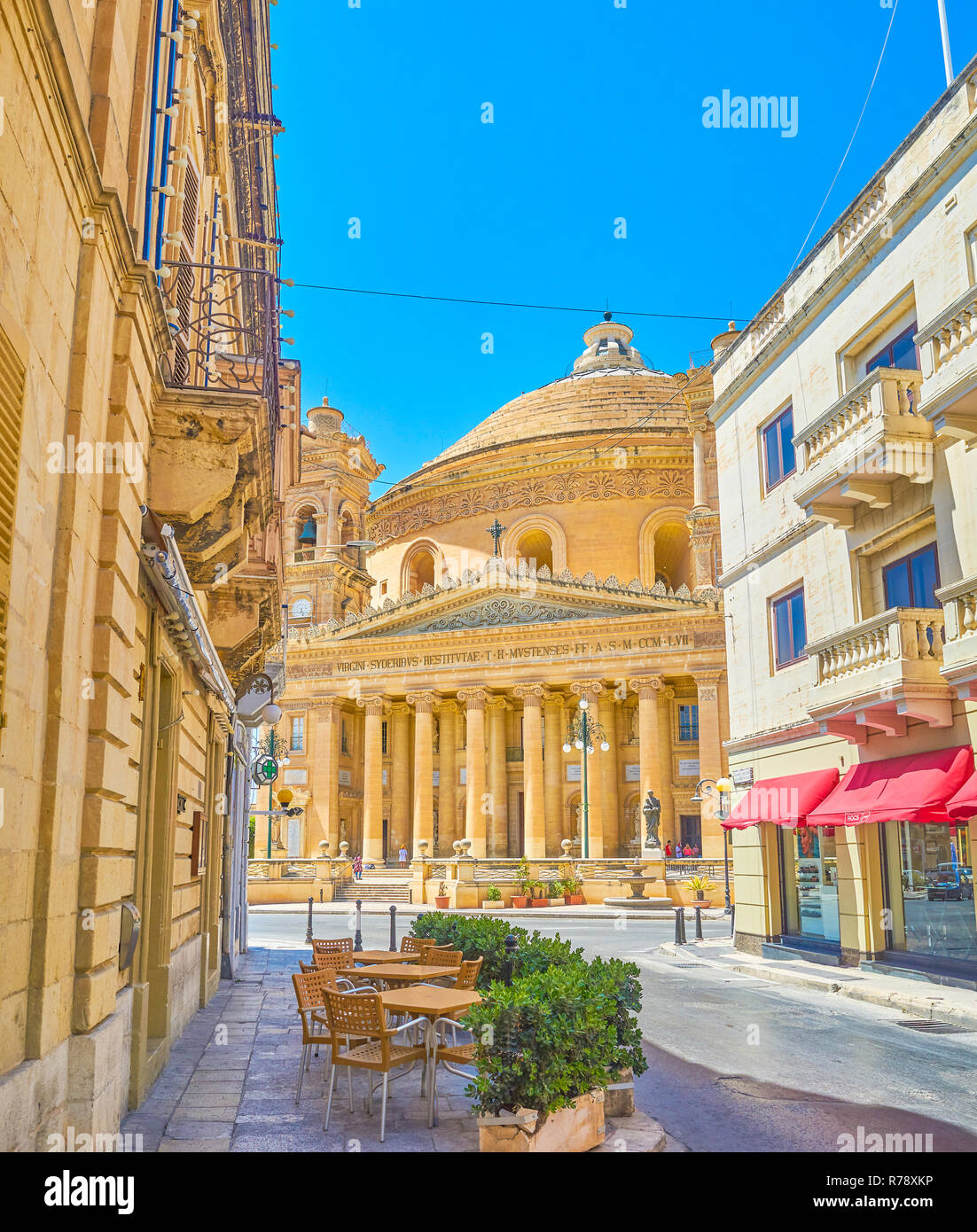 MOSTA, MALTE - Juin 14, 2018 : l'étroite rue ombragée avec café en plein air ouvre la vue sur occupation carré rotonde avec son principal point de repère - Basilique du Banque D'Images