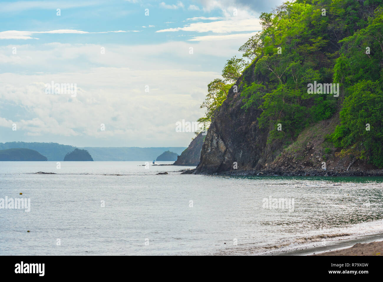 Le feuillage des arbres et se développer de très vieux rocher sur une pente raide, la hausse que les frontières qui affleurent une plage au Costa Rica. Bateau va le long de la côte rocheuse Banque D'Images