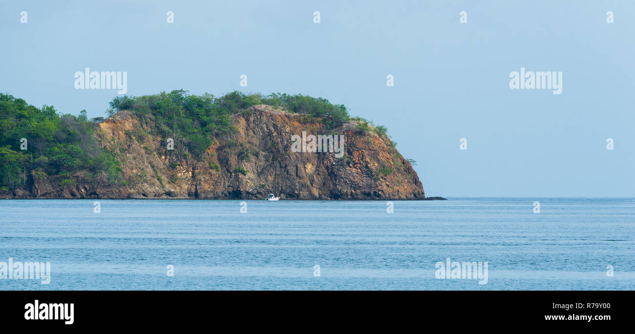Le feuillage des arbres et se développer de très vieux rocher sur une pente raide, la hausse que les frontières qui affleurent une plage au Costa Rica. Bateau va le long de la côte rocheuse Banque D'Images