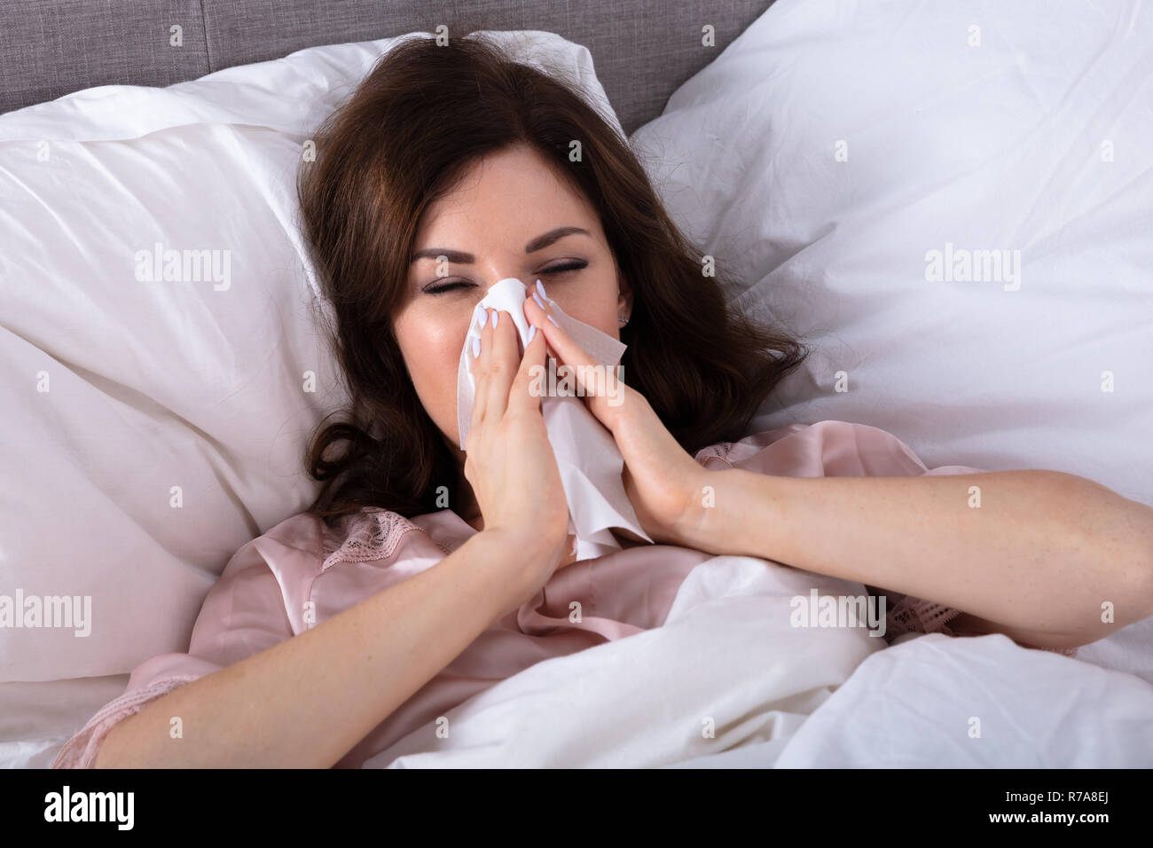 Sick Young Woman Lying On Bed éternuer dans un mouchoir Banque D'Images