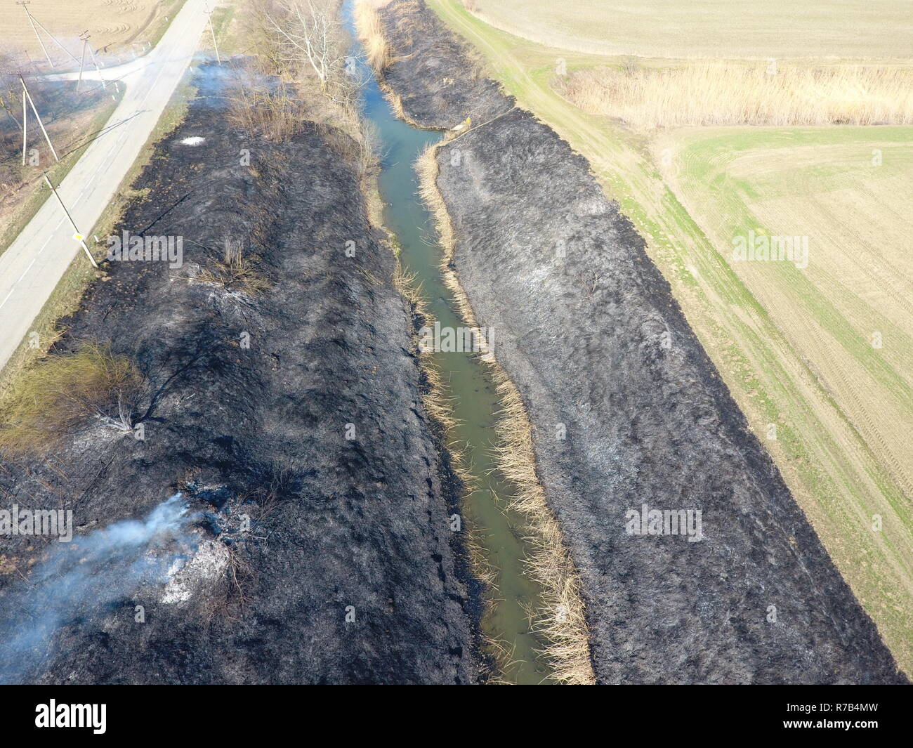 La combustion de l'herbe sèche le long du canal d'irrigation. La fumée et la flamme de l'herbe sèche. Brûlé de l'herbe sèche. Banque D'Images
