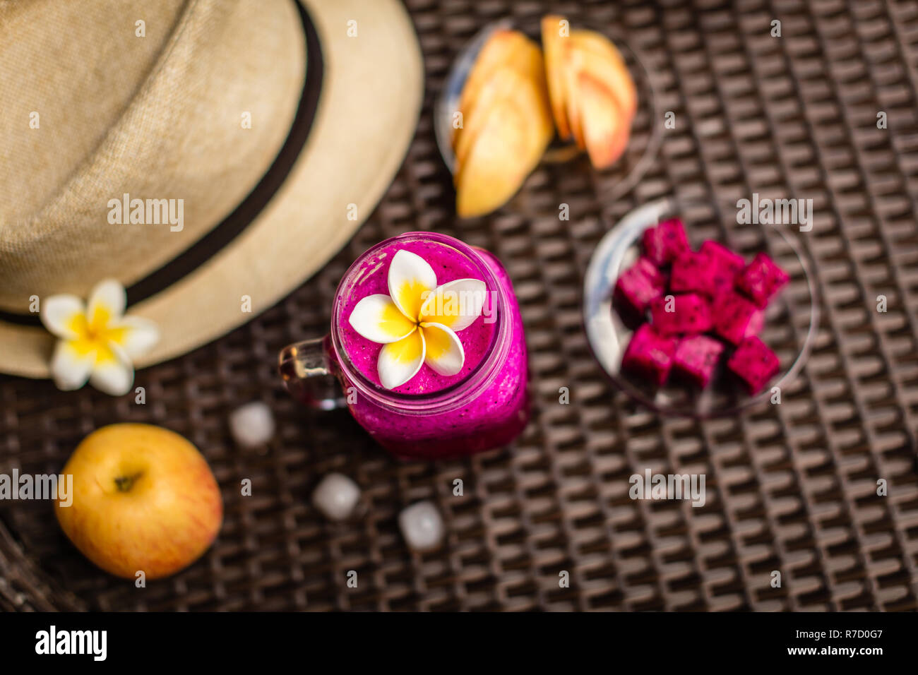 Fruit du dragon rouge et le jus de pomme dans un verre décoré de Plumeria flower. Hat, pommes, fruits du dragon coupés, des cubes de glace sur la surface sombre. Vue d'en haut. Banque D'Images