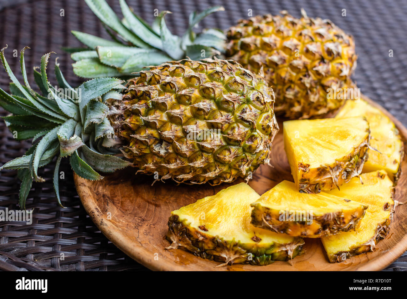 Ensemble de deux gros ananas et couper des morceaux sur un plateau de bois rond, brun foncé sur la surface. Vue de côté. Banque D'Images