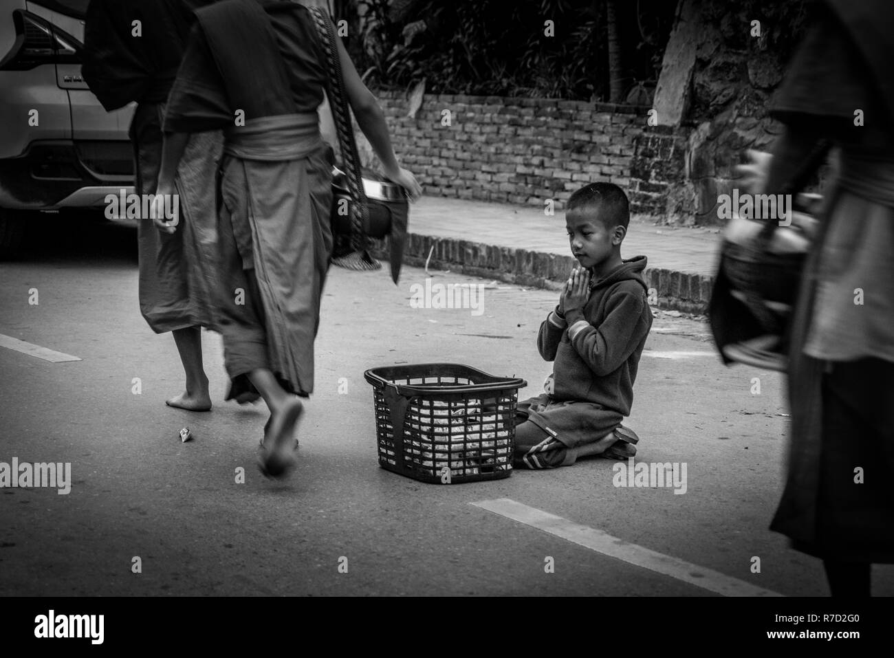 Luang Prabang. Le 6 février 2016. Un enfant est assis tranquillement et vous demande les aumônes des moines comme ils le matin passby à Luang Prabang Banque D'Images