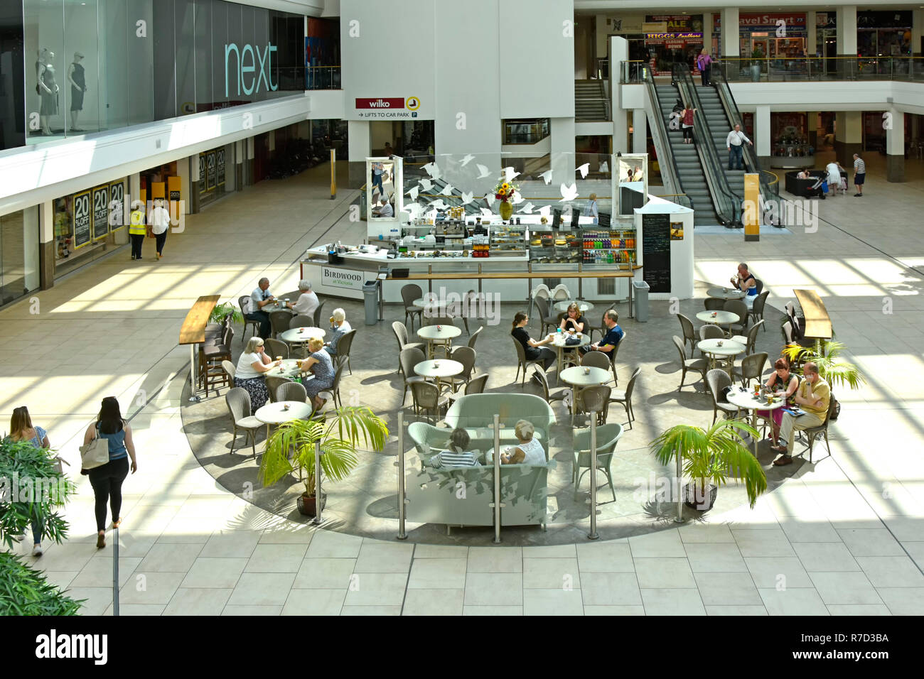 De haut en bas du centre commercial Mall shoppers dans & les gens assis à des tables de café à côté de la sortie d'une boutique de vêtements escalator au-delà de Southend Essex UK Banque D'Images